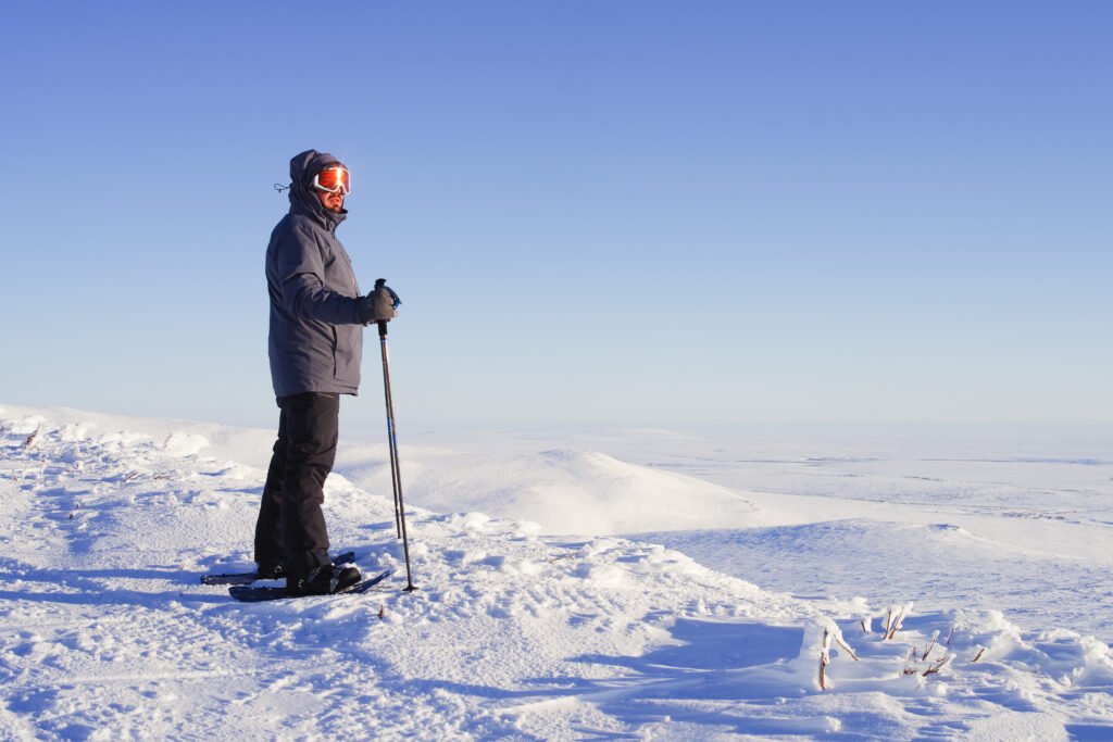 Photograph of Dr. Gustaveson with walking sticks and snow shoes on subarctic tundra terrain.