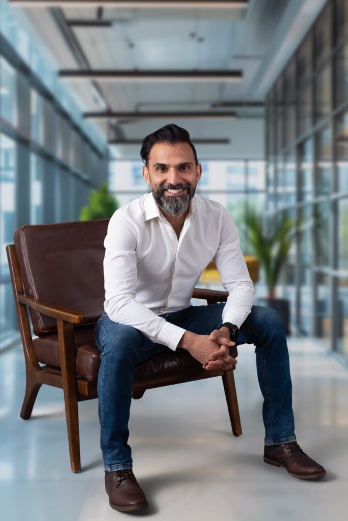 A photograph of Dr. Fathi sitting in a professional environment. He is a male seated on a wooden chair with brown leather padding smiling with brown hair and bard with gray in his beard.